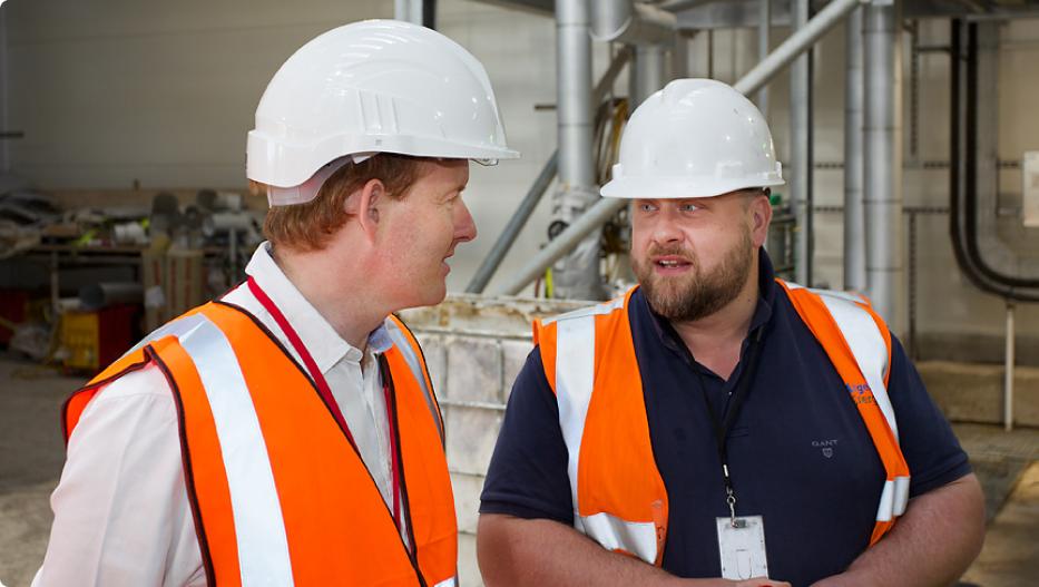 2 men in high-visibility jackets and and hardhats talking while in a biofuel plant 2
