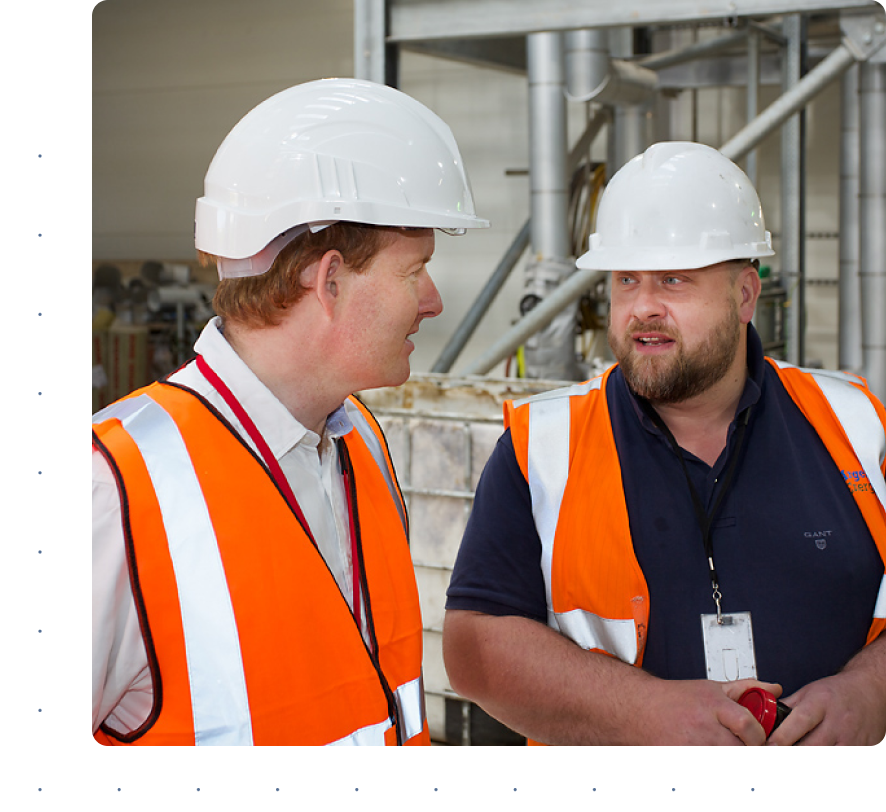 2 men in high-visibility jackets and and hardhats talking while in a biofuel plant