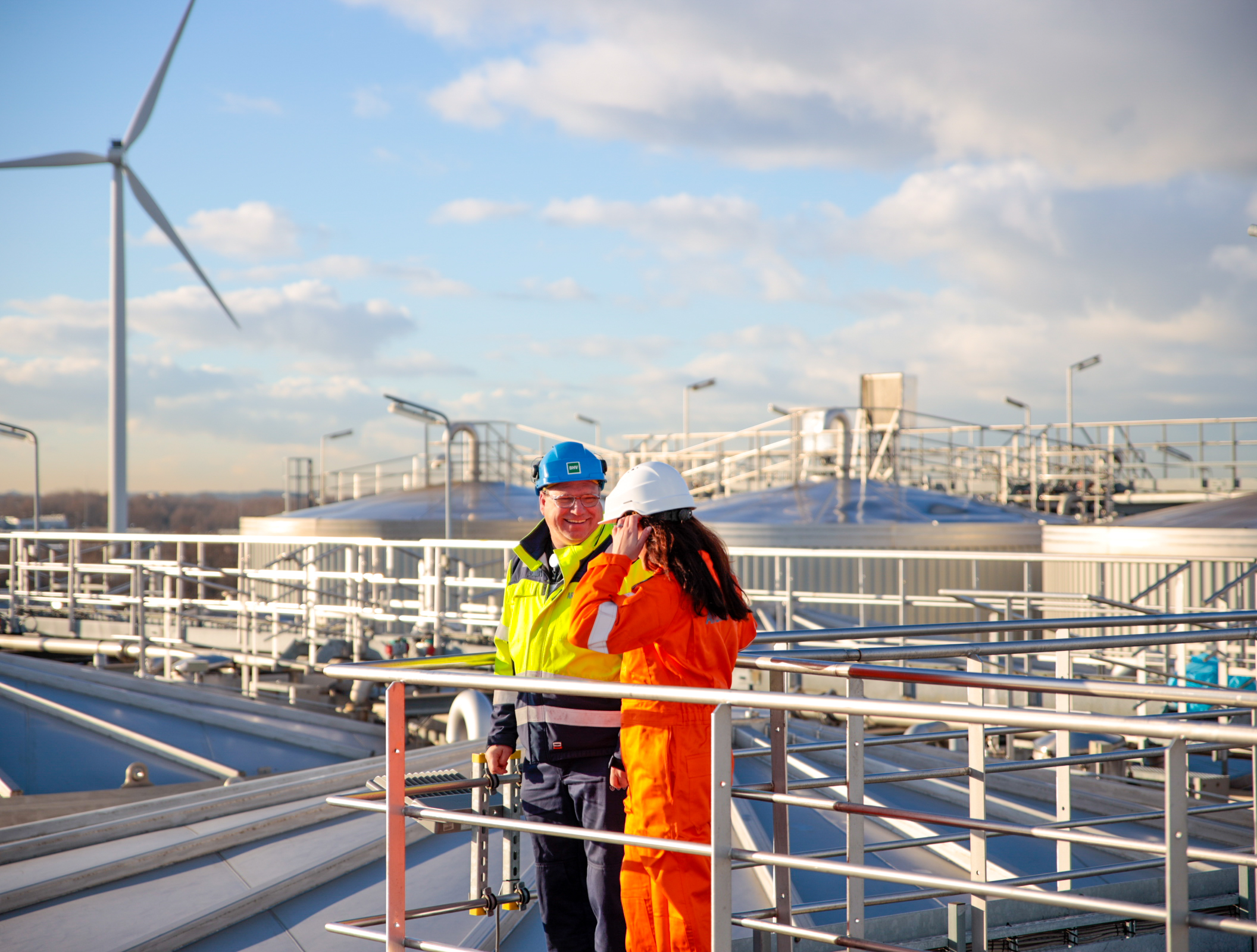 2 employees in high-visibility jackets and hardhats talking while in a biofuel plant